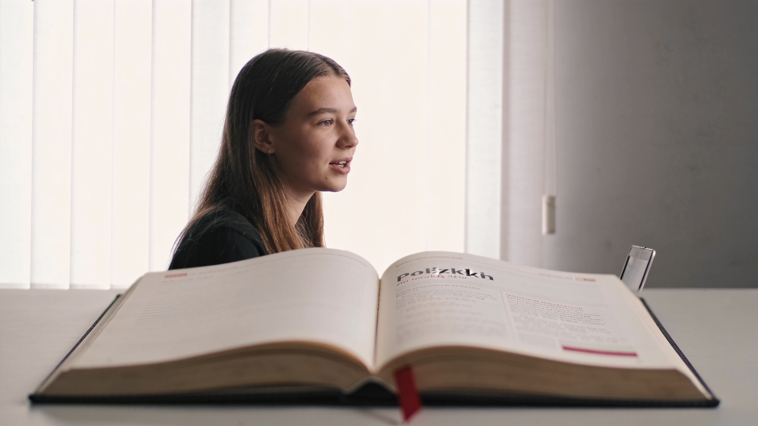 Learner practicing a Polish vowel at an editorial desk beside an open notebook and crimson bookmark