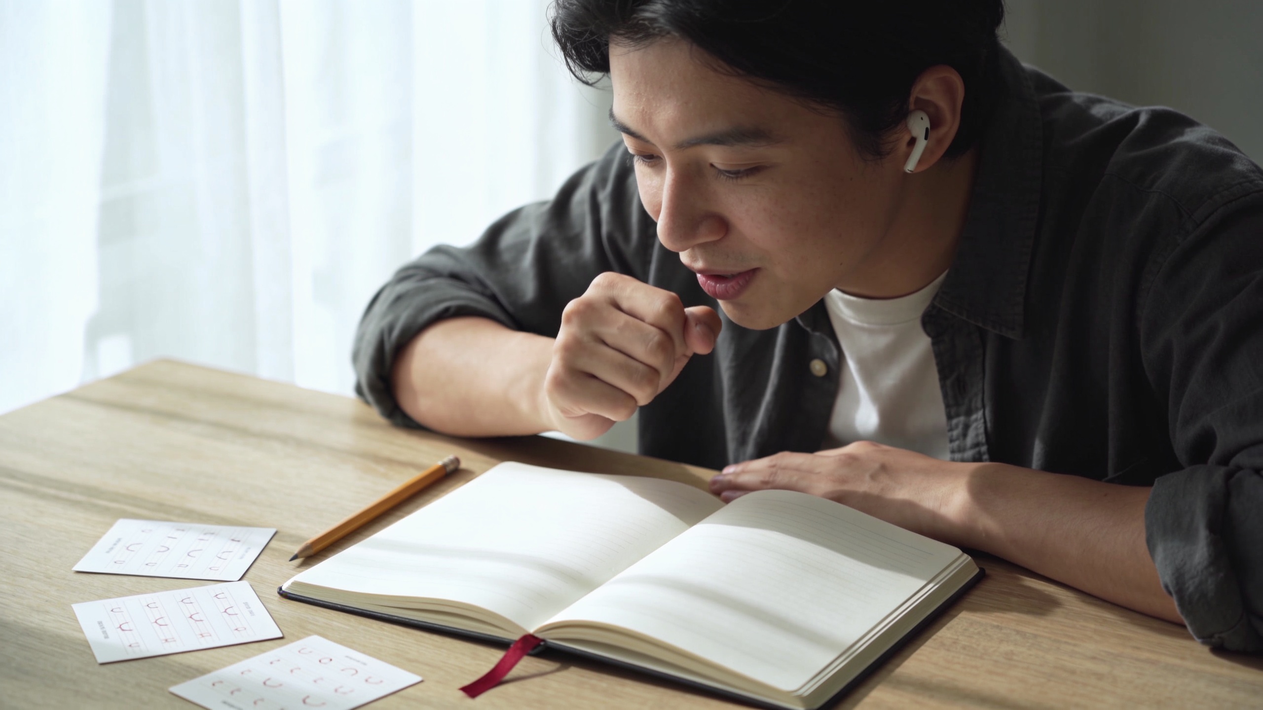 Learner practicing Polish pronunciation at a desk with an open notebook and a crimson bookmark